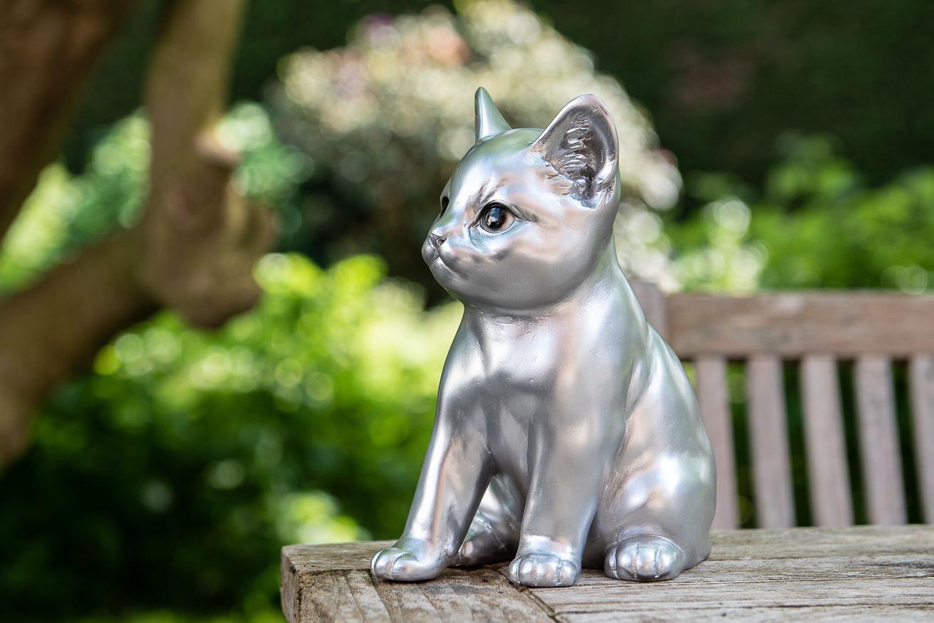 Statue einer modernen silbernen Katze, die auf einem hölzernen Gartentisch steht Garden ID
