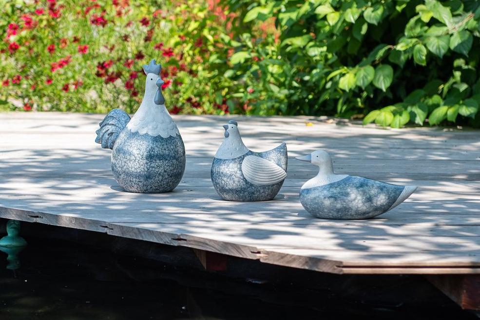 Ornamenten met blauwsteeneffect zoals een haan, een hen en een eend op een houten terras bij een vijver Garden ID