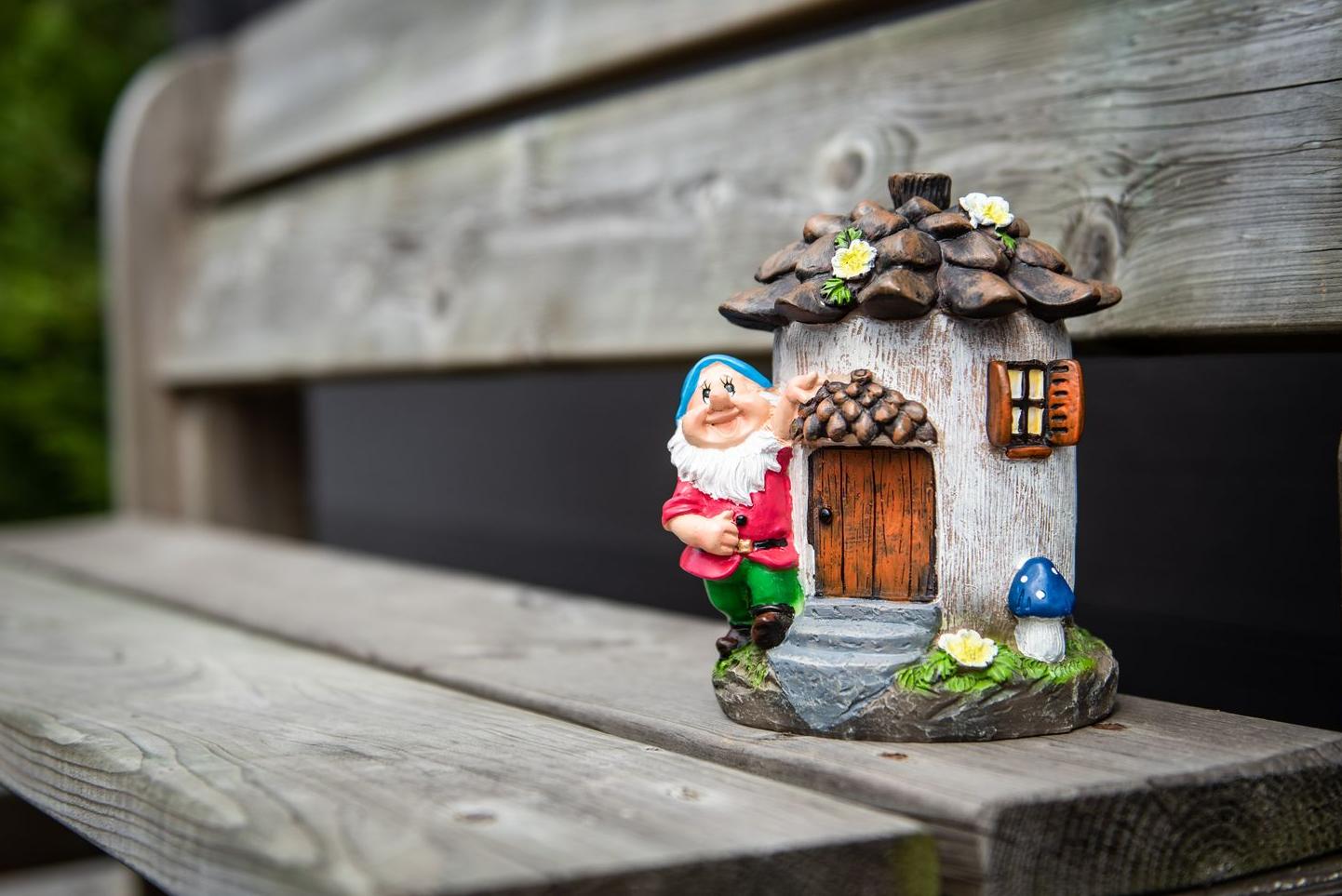 Ein Gartenzwerg mit seinem kleinen Haus auf einer Holzbank Garden ID