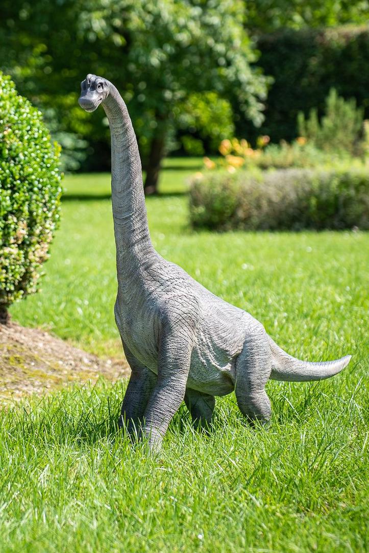 Eine hyper-realistische Statue eines Brachiosaurus-Dinosauriers, der in einem Garten spazieren geht Garden ID