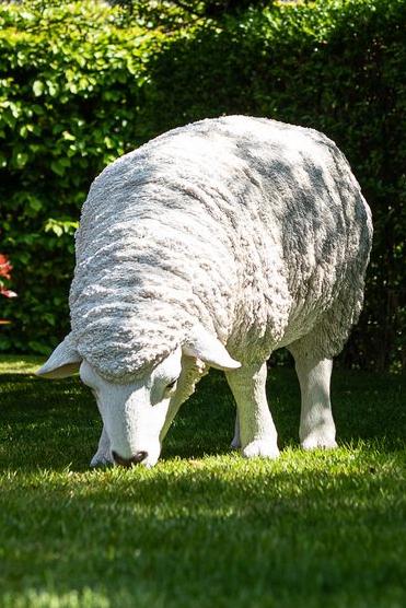 A hyper-realistic statue of a white sheep grazing grass in a garden Garden ID